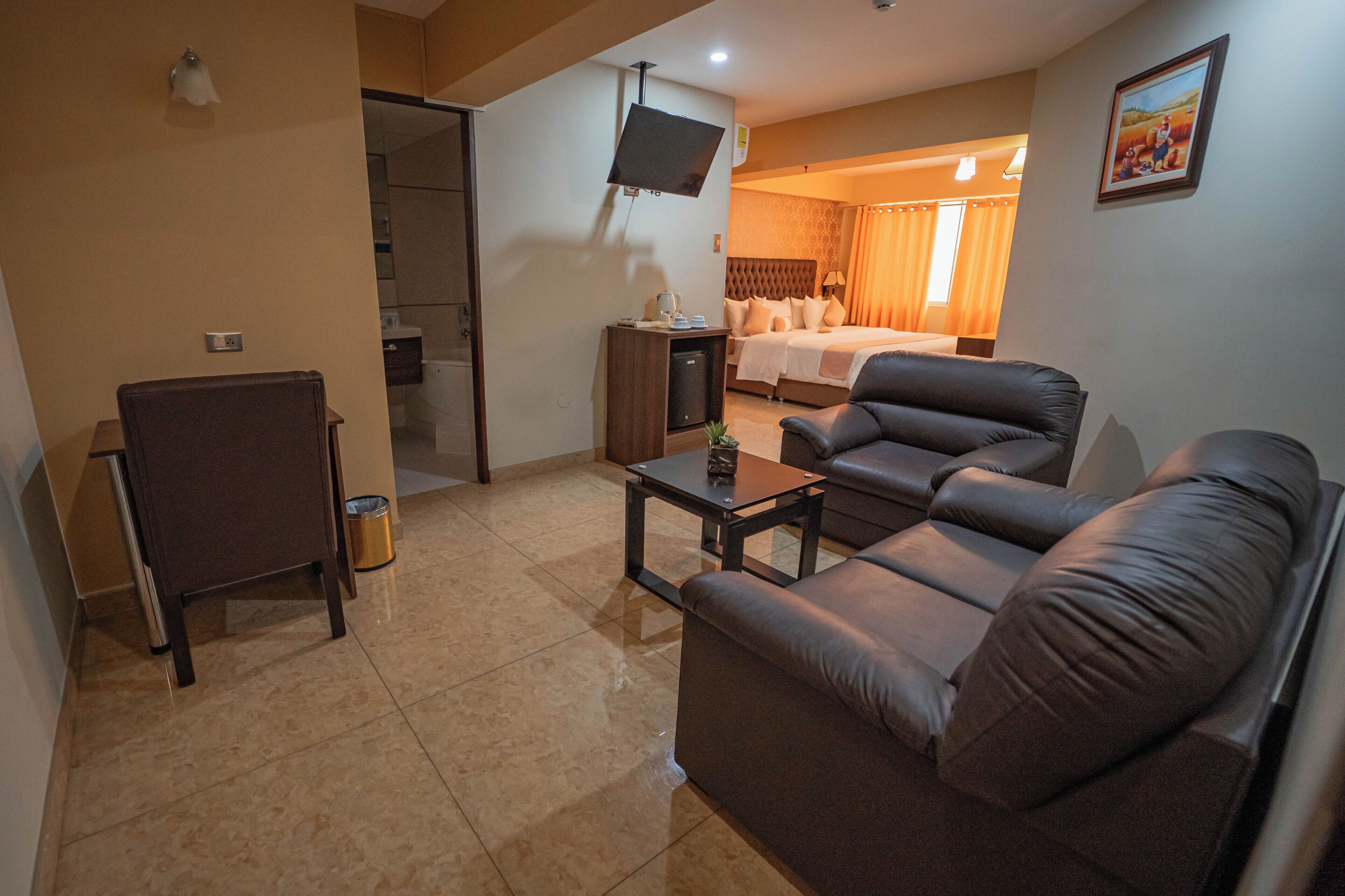 A hotel room with a sofa, a small table, a TV mounted on the wall, and a bed with curtains.