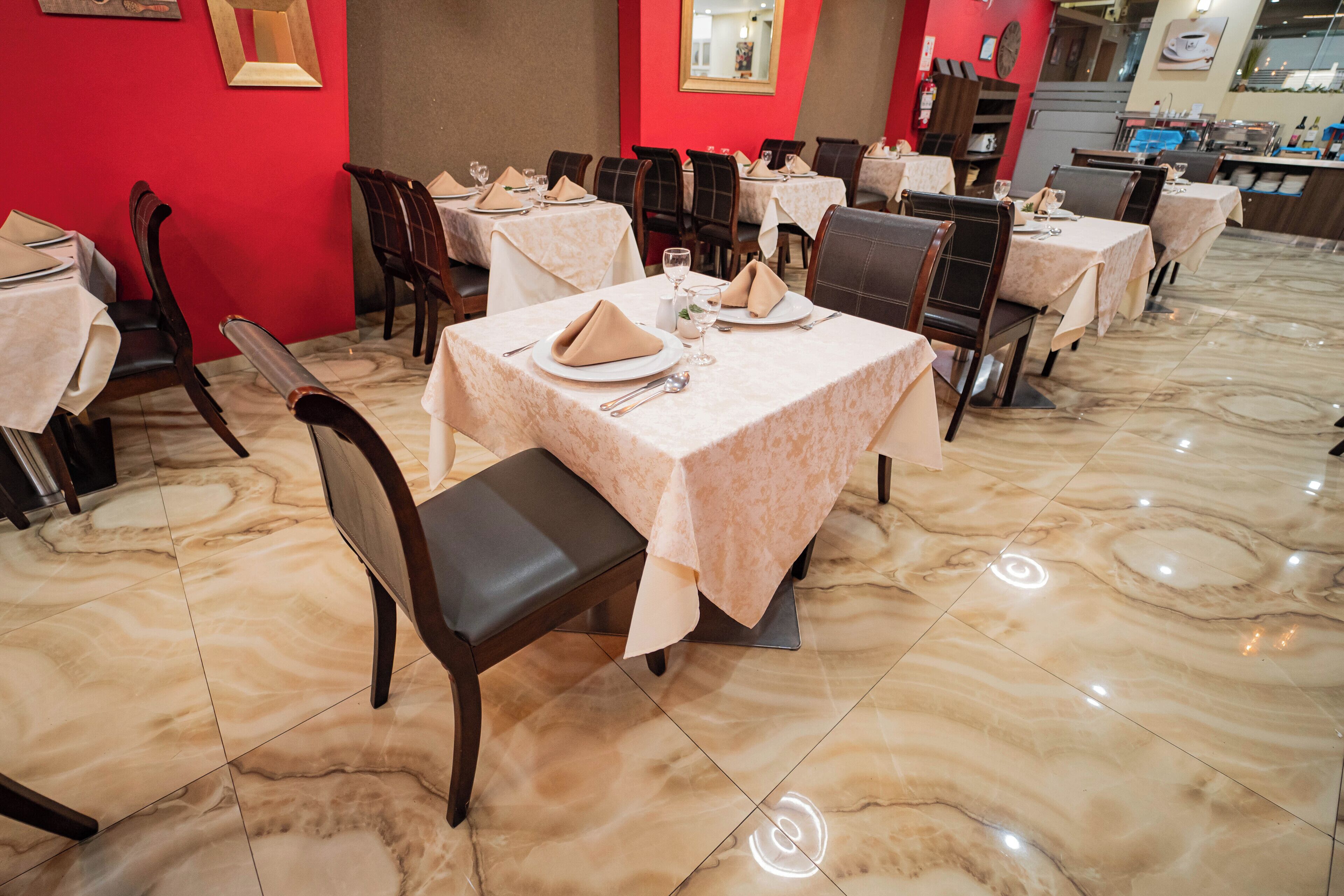 Un restaurante con suelo de mármol, mesas ordenadas con manteles blancos y sillas de madera oscura.