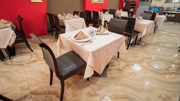 Un restaurante con suelo de mármol, mesas ordenadas con manteles blancos y sillas de madera oscura.