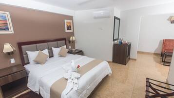 Habitación de hotel con una cama grande, una mesita de noche, un escritorio, una silla y un espejo.