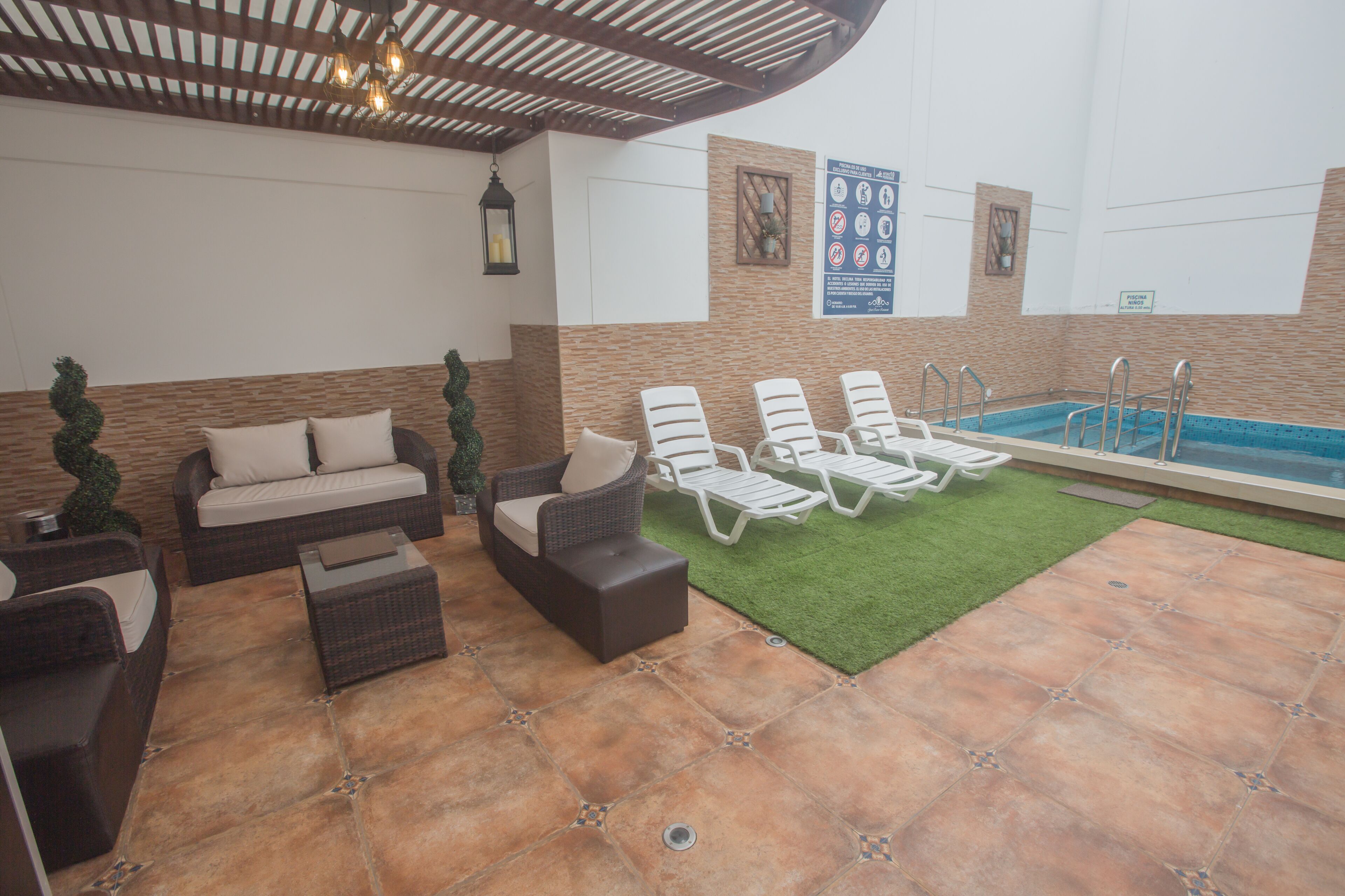 A covered outdoor lounge area with wicker furniture, a pool, and a green artificial turf.