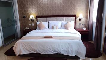 A modern hotel room with a large bed, two bedside tables with lamps, a dark rug, and a patterned wall.