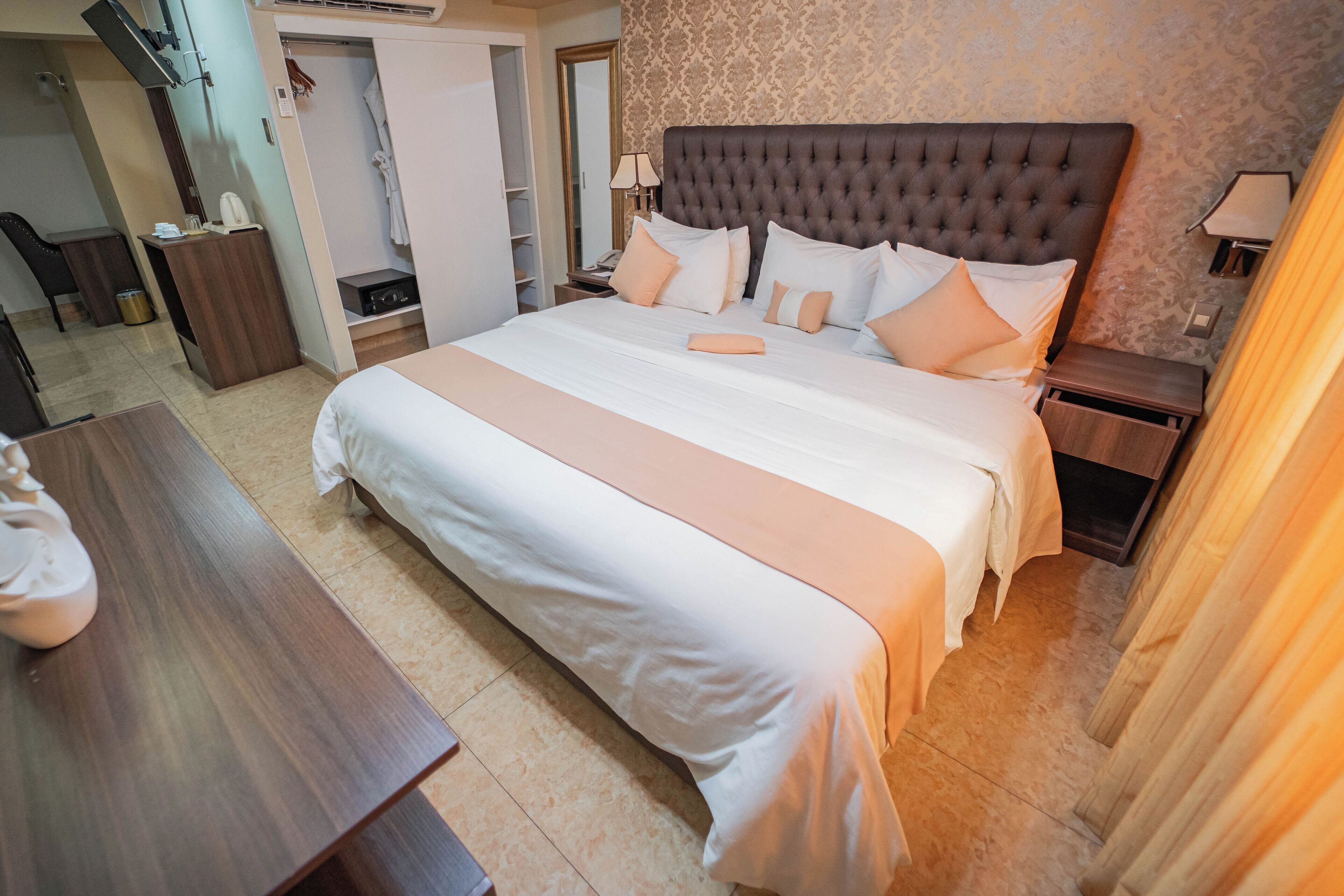 Una habitación de hotel con una cama grande, mesitas de noche, un escritorio y un armario.