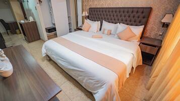Una habitación de hotel con una cama grande, mesitas de noche, un escritorio y un armario.
