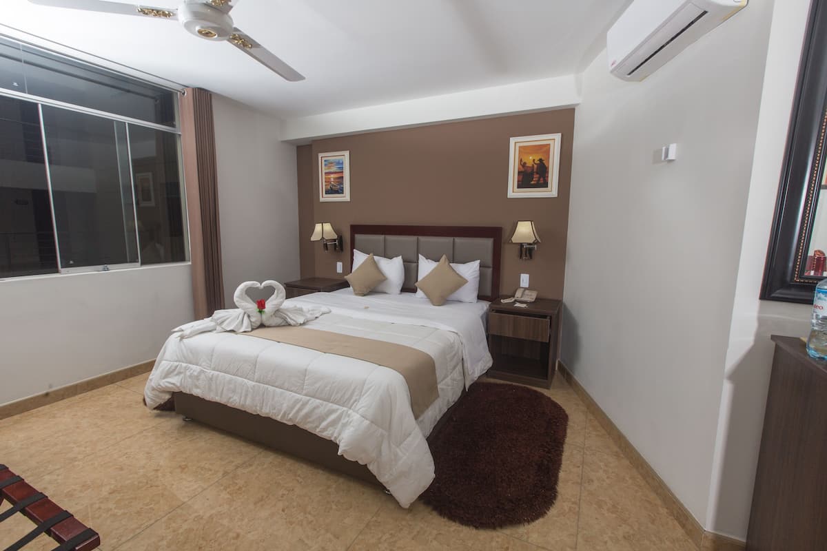 A hotel room with a large bed, two bedside tables, a ceiling fan, and a large window with curtains.
