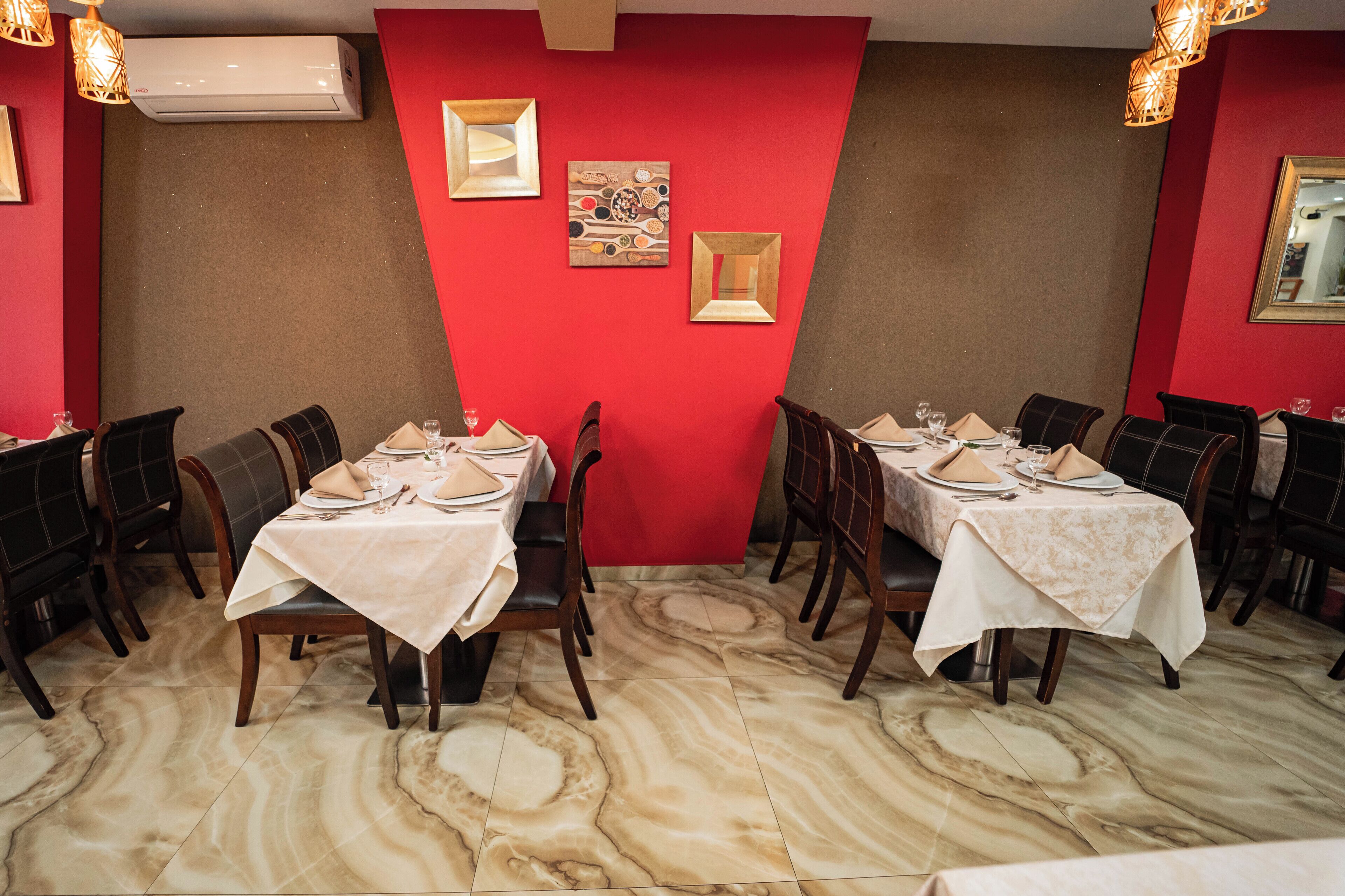 Un restaurante con piso de mármol, paredes rojas y varias mesas de comedor con manteles blancos y sillas.