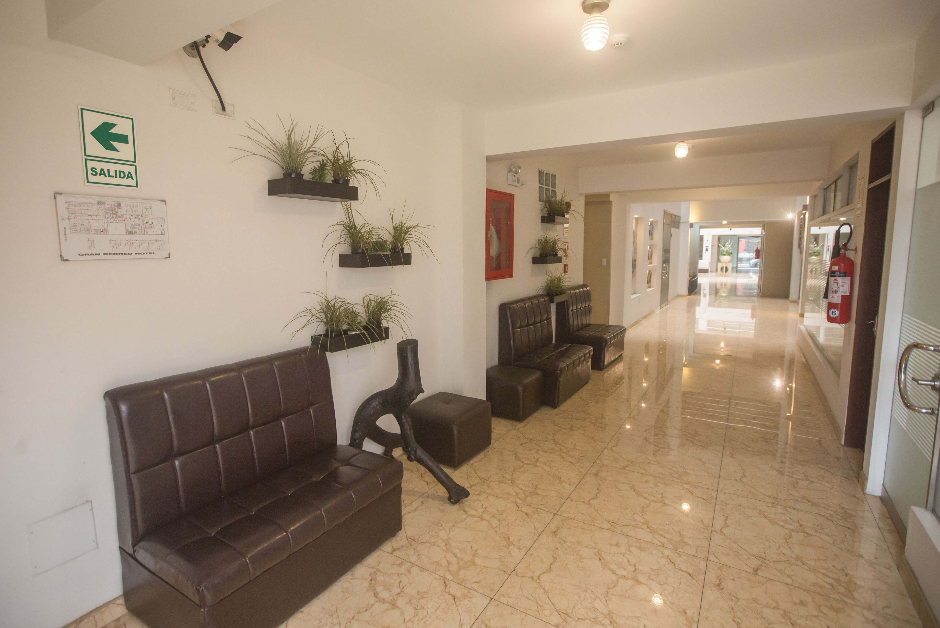 Un vestíbulo de hotel con un sofá de cuero marrón, plantas en macetas, un extintor y un letrero de indicaciones.