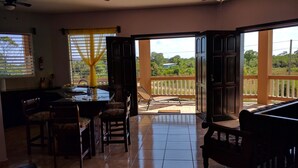 A spacious living area with a kitchen, dining table, and chairs. There is a sliding glass door leading to a balcony with a view of greenery. - Savannah Sand Dollar (Hopkins)