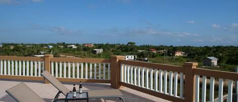 A balcony with two lounge chairs and a small table, overlooking a residential area with houses and greenery.