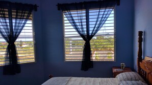 A bedroom with a bed, two windows with curtains, a wooden headboard, and a nightstand with a lamp. - Savannah Sand Dollar (Hopkins)