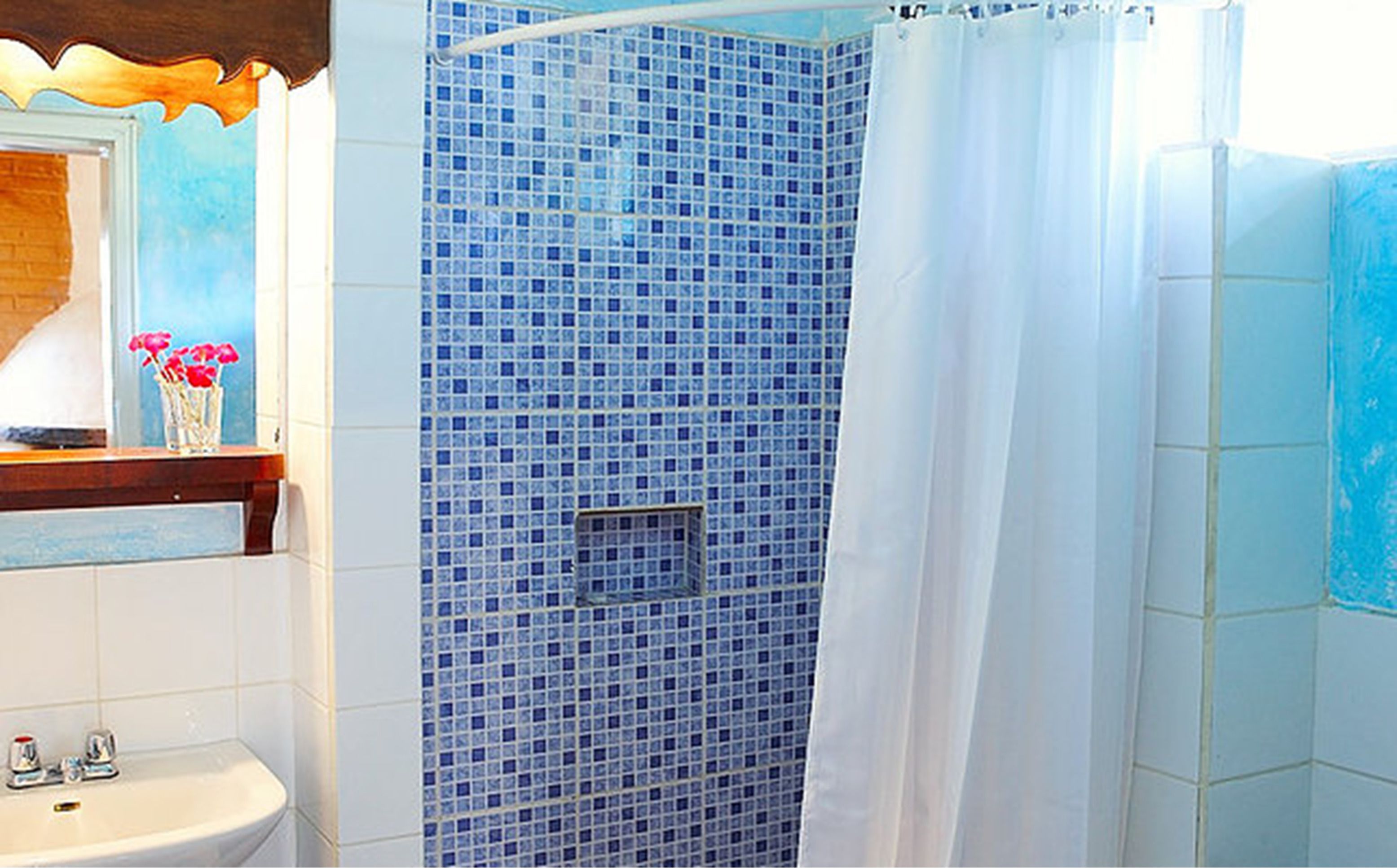 A bathroom with a blue-tiled shower, a white sink, and a mirror with a wooden frame.