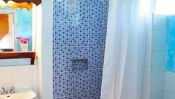 A bathroom with a blue-tiled shower, a white sink, and a mirror with a wooden frame.