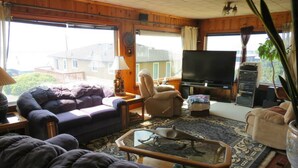 Ein Wohnzimmer mit einer Couch, einem Sessel und einem Couchtisch. Ein Fernseher und ein großes Fenster sind ebenfalls vorhanden.
