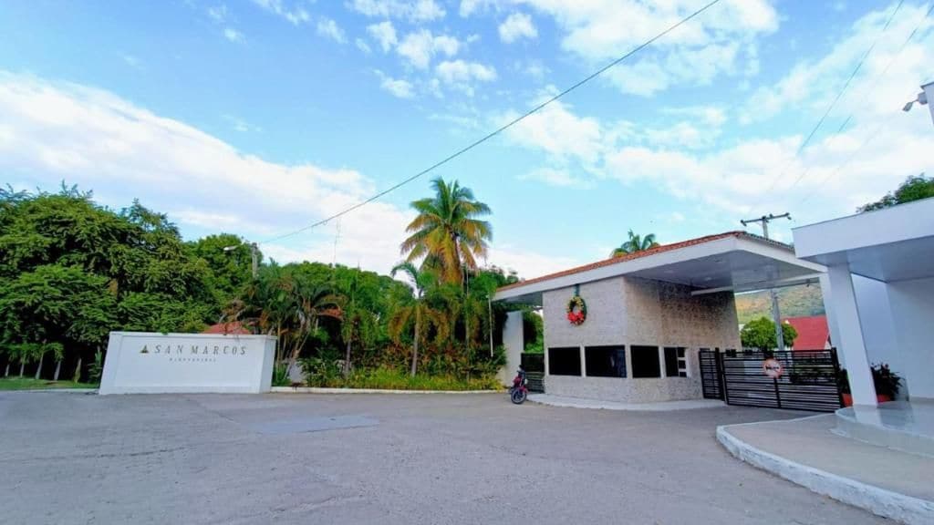 A gated entrance with a sign reading 'San Marcos,' a covered area with a roof, and a motorcycle parked in front.