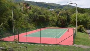 Una cancha de tenis al aire libre rodeada de vegetación y colinas.