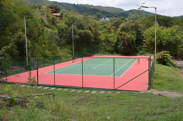 Una cancha de tenis al aire libre rodeada de vegetación y colinas.