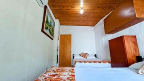 A room with two beds, a wooden ceiling, a door, and a framed picture on the wall.
