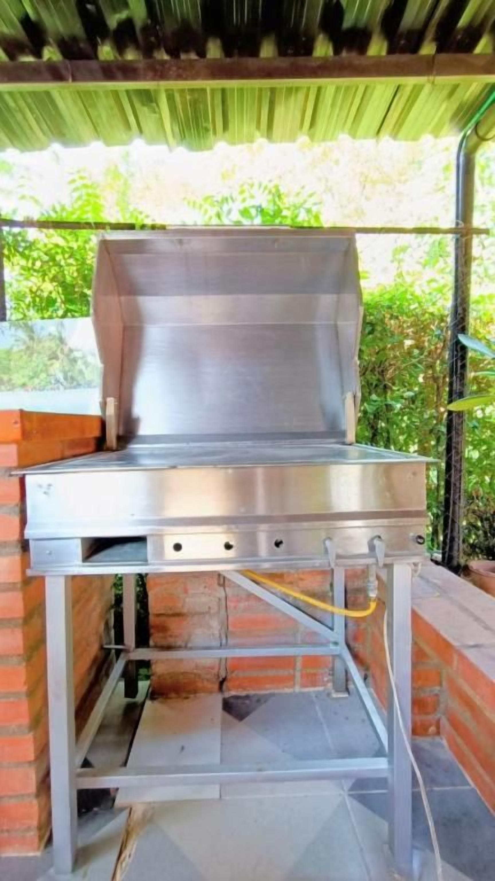 En udendørs grill i rustfrit stål med låg, monteret på en konstruktion af mursten og metal.