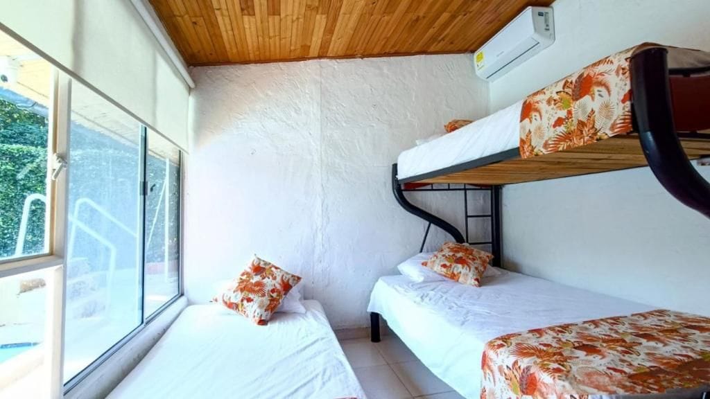 Une chambre avec un lit superposé, une fenêtre, des murs blancs et un plafond en bois.