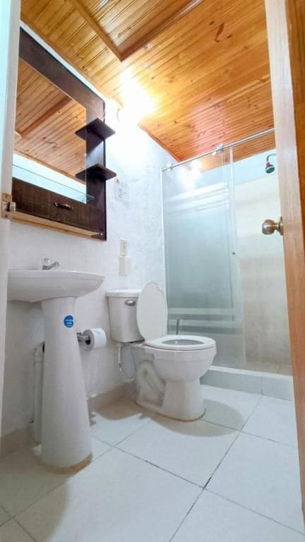 A bathroom with a wooden ceiling, a white sink, a toilet, and a glass shower enclosure.