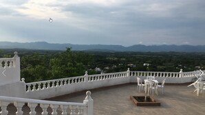 Una terraza con vistas a montañas distantes, barandas blancas y mobiliario exterior.
