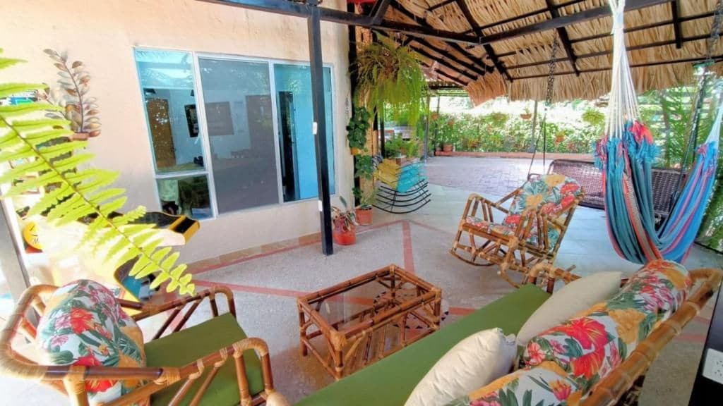 A covered outdoor seating area with wicker furniture, a hammock, and potted plants.