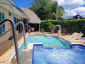 Una piscina con hidromasaje, sillas de descanso y una estructura de techo de paja.
