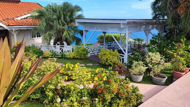Un jardín con un pabellón, palmeras y vistas al mar.