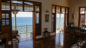 Amplia sala de estar con vista al océano, pisos de madera y un comedor con sillas y mesa.