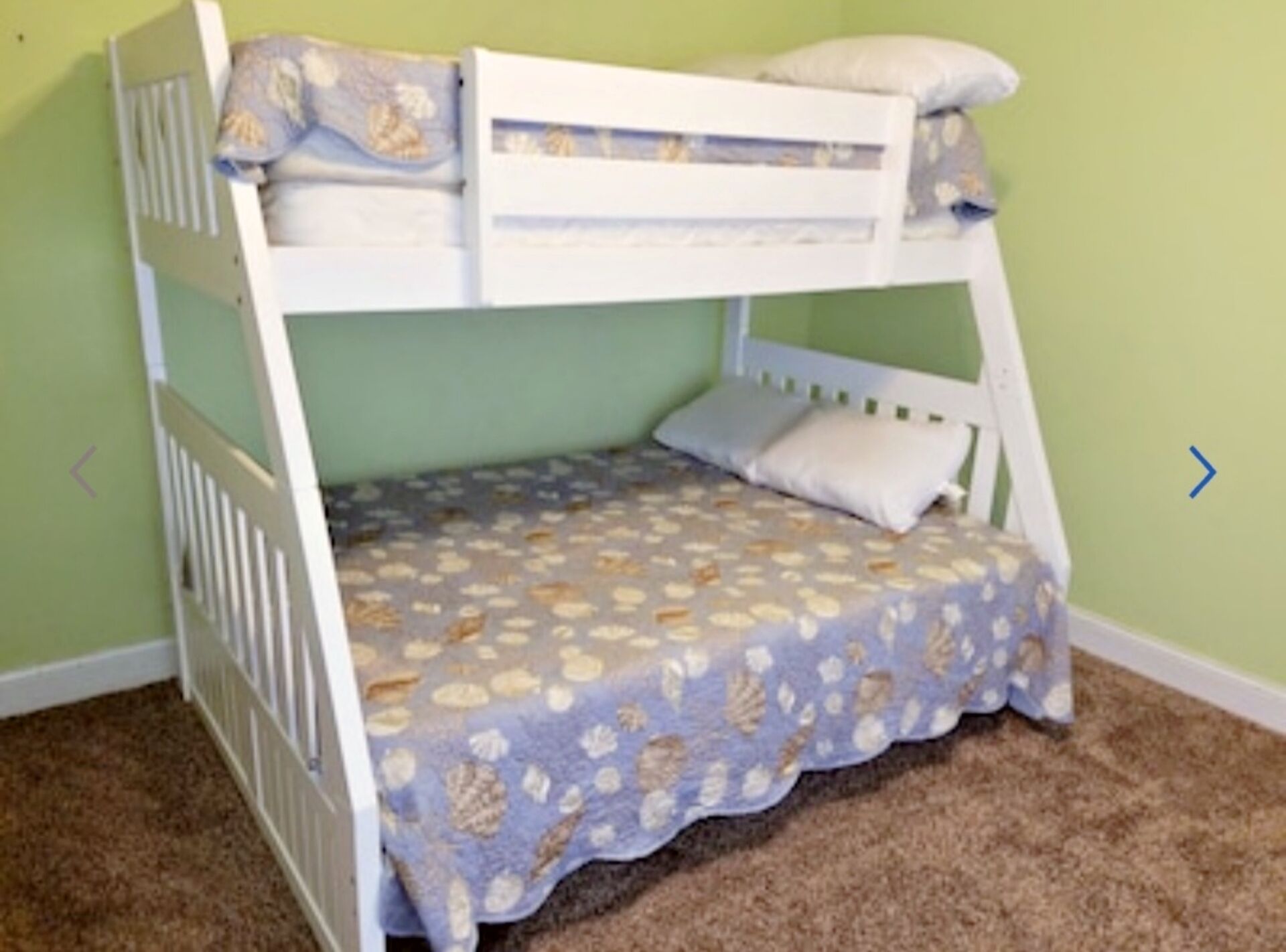 A bunk bed with a patterned bedspread and pillows, set against a green wall.