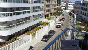 A multi-story residential building with balconies, a street with parked cars, and a clear sky. - Apartment with a balcony just one block from Forte beach! (Cabo Frio)
