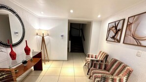 A modern living room with a glass coffee table, red vases, a floor lamp, and patterned armchairs. - Apartment with a balcony just one block from Forte beach! (Cabo Frio)