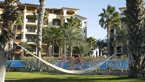 A hotel with multiple balconies, palm trees, and a hammock in the courtyard. - BeachFront, Golf, Heated pool, Tennis,Netflix, Gym, Pickleball (La Paz)