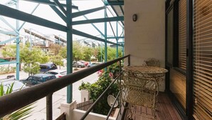 A balcony with a metal railing, a wicker table, and a view of a street with cars and buildings. - Charming Townhouse in the Heart of Fremantle (Fremantle)
