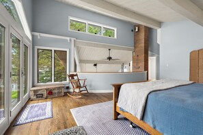Un dormitorio con cama, una mecedora, un escritorio y ventana con vistas a la vegetación.