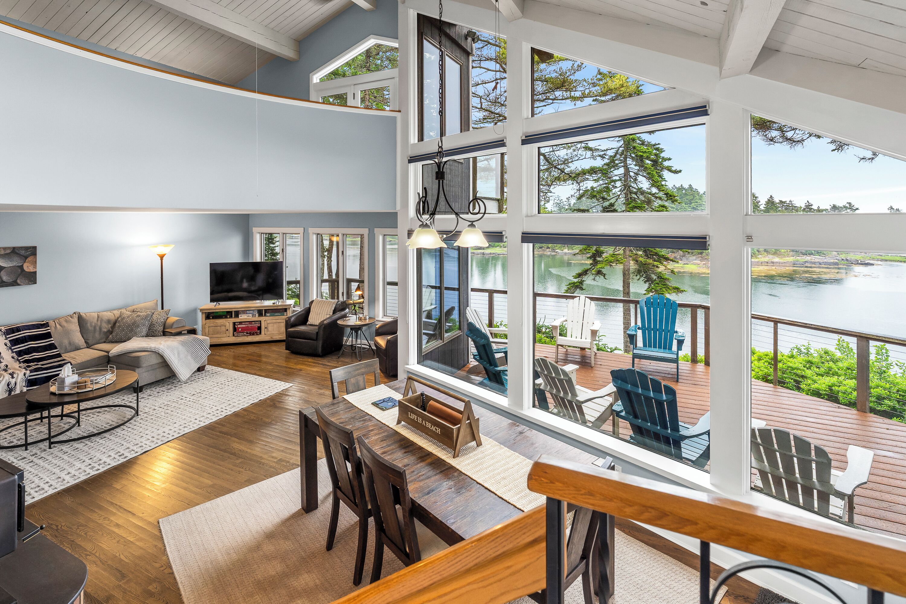 A spacious living area with a large window overlooking a lake, a dining area with wooden furniture, and a cozy seating area with a fireplace.