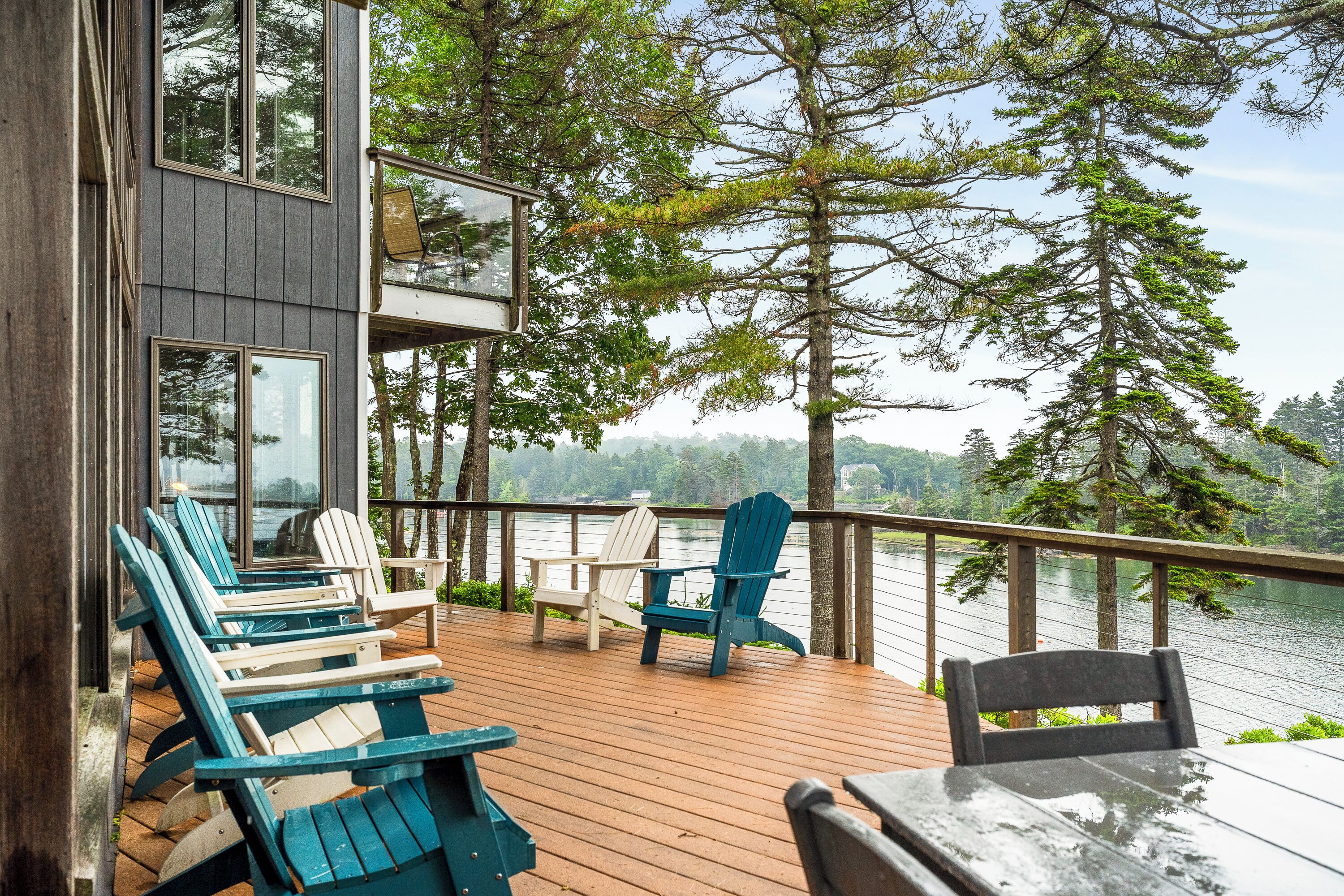 A deck with chairs and a table overlooking a lake, surrounded by trees.