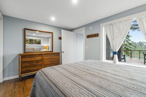 Et soveværelse med seng, kommode, spejl og en balkon med gardiner.