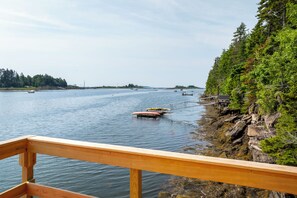 En træterrasse med udsigt over et roligt vandareal med både og en skovklædt kystlinje.