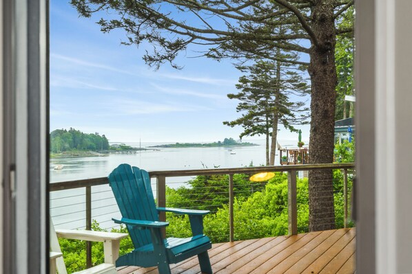 A deck with a view of a body of water, a chair, and a tree.