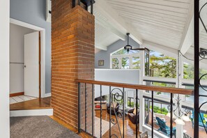 A spacious balcony with a wooden railing, a brick fireplace, and a view of the outdoors.
