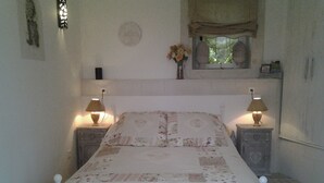 Een slaapkamer met een bed, twee nachtkastjes met lampen, een raam met uitzicht en een wandklok.