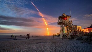 A beach with a lifeguard tower, a sunset, and a clear sky.