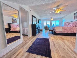 Une chambre spacieuse avec un grand lit, une commode, une chaise et un bureau. Elle dispose d’un balcon avec vue sur l’océan.