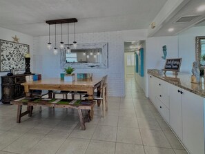 Une cuisine moderne avec une table à manger en bois, des luminaires suspendus et un mur de briques blanches derrière le plan de travail.