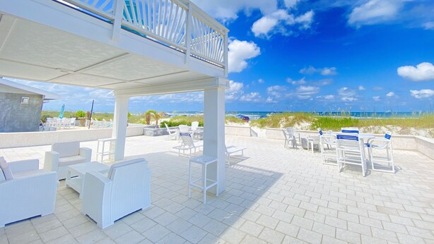 A covered outdoor seating area with white wicker furniture and a view of the beach.
