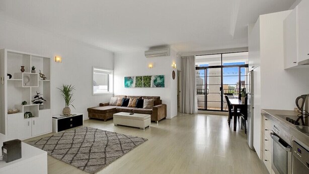 A modern living room with a sofa, a coffee table, and a rug. There is a dining area with a table and chairs. The room has white walls and a large window. - Ultimate 2-Bed Apartment in Surry Hills - Ultimate Convenience (Surry Hills)