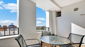 A balcony with a glass table and chairs, a view of the cityscape, and a window with blinds. - Ultimate 2-Bed Apartment in Surry Hills - Ultimate Convenience (Surry Hills)