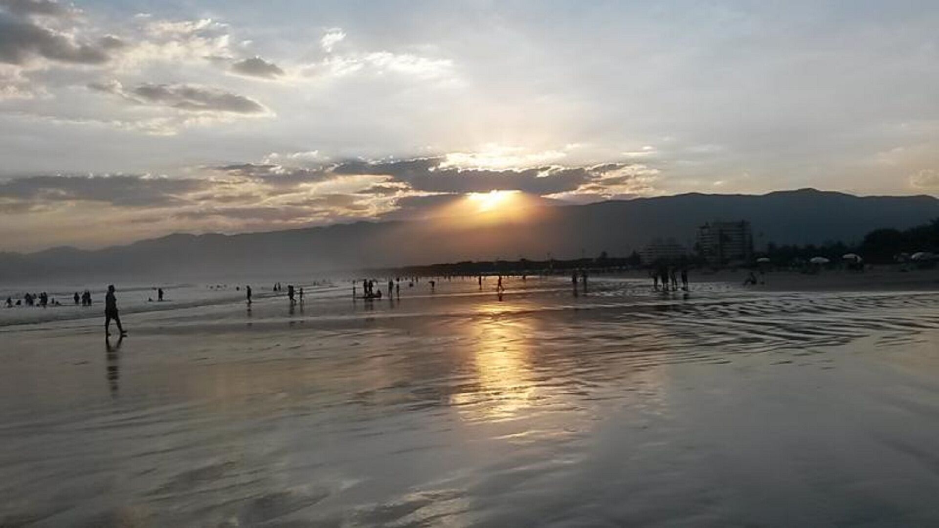 Une plage où l’on voit des gens se promener et se tenir debout, avec un coucher de soleil en arrière-plan.