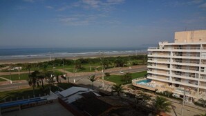 A hotel with a pool, a view of the beach, and a road in the foreground.
